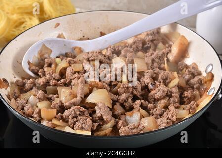 Cottura a vapore di manzo e cipolle in una padella di ghisa con spaghetti sullo sfondo Foto Stock