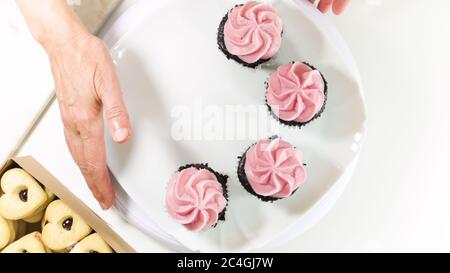 Cupcake al cioccolato con crema di lamponi e biscotti a forma di cuore si chiudono su sfondo bianco, vista dall'alto. Foto Stock