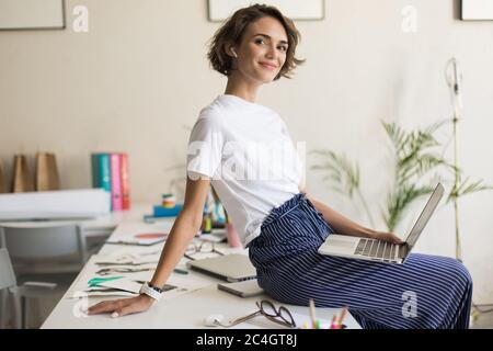 Donna giovane sorridente con capelli ricci corti negli auricolari wireless Foto Stock