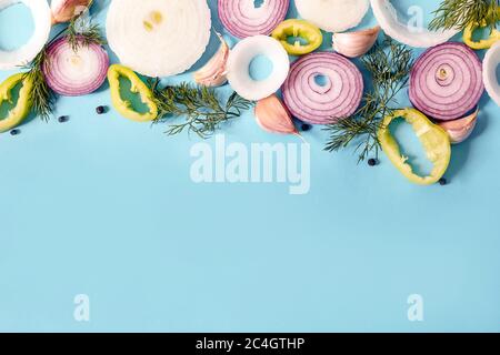 Anelli di cipolla su sfondo blu. Cipolla biologica fresca, aglio e peperone, sedano, verdure aneto con spazio per la copia. Sfondo vegetariano Foto Stock