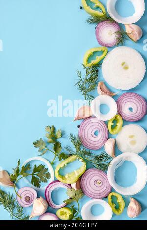 Anelli di cipolla su sfondo blu. Cipolla biologica fresca, aglio e peperone, sedano, verdure aneto con spazio per la copia. Sfondo vegetariano Foto Stock