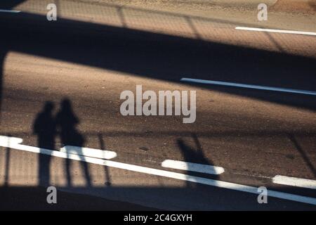 Ombre di persone su un passo pedonale sopraelevato proiettato su una strada vuota sotto. Foto Stock