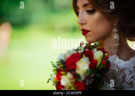 La sposa in un abito da sposa bianco tiene un bouquet sullo sfondo di un parco verde Foto Stock