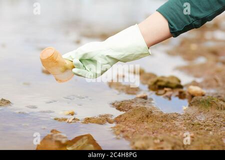 Primo piano di donna in guanti protettivi che raccolgono i rifiuti sul fiume Foto Stock