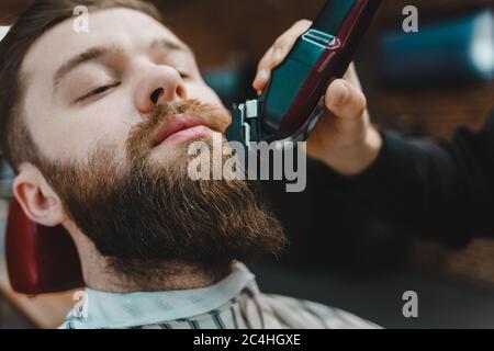 Barber master taglia una barba da vicino a un cliente Foto Stock