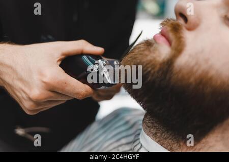 Barber master taglia una barba da vicino a un cliente Foto Stock