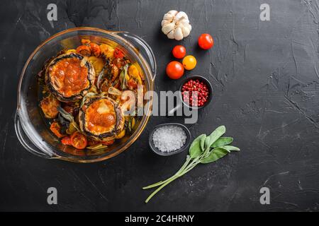 Funghi Portobello, cotti con ingredienti formaggio cheddar, pomodori ciliegini e salvia in vaso di vetro su sfondo nero pietra spazio vista dall'alto per il testo Foto Stock