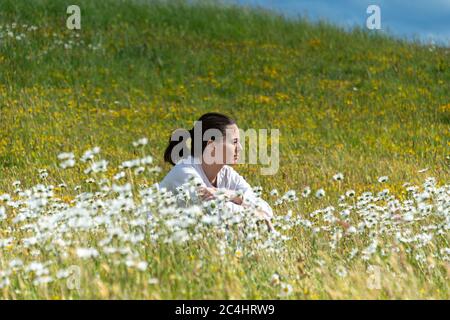 donna seduta in un campo di margherite. Foto Stock