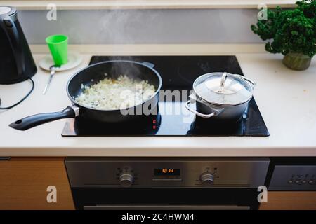 Le cipolle tritate finemente vengono fritte in una padella. Friggere la padella e la padella su una stufa a induzione. Foto Stock