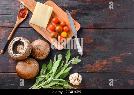 Funghi Portabello ingredienti per la cottura, formaggio cheddar, pomodori ciliegini e salvia su vecchio tavolo scuro, spazio vista dall'alto per il testo Foto Stock