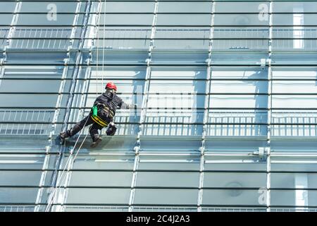 Pulitore per vetri con attrezzatura di sicurezza sulla facciata in vetro lucido di un grattacielo Foto Stock