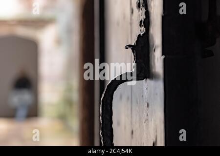 Fuoco basso di una porta medievale di legno e di un latch di ferro in un popolare sito turistico. Un visitatore può essere visto entrare in un arco lontano. Foto Stock