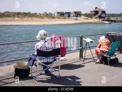 Due artisti lady sulla banchina a Mudeford che si affaccia sulla spiaggia e il mare Foto Stock