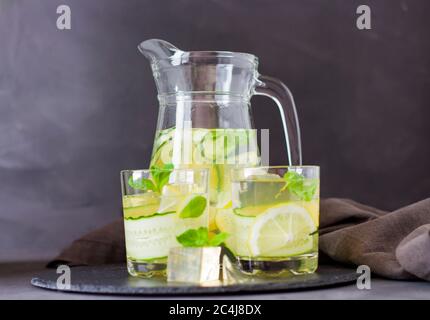 rinfrescante bevanda estiva. Bere con ghiaccio, limone e cetriolo con menta. un decanter e due bicchieri con una bevanda rinfrescante. copyspace Foto Stock