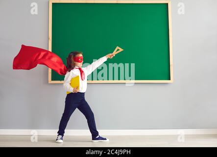 Ritorno a scuola. Studentessa in un costume da supereroe sullo sfondo di una scuola verde in classe. Foto Stock