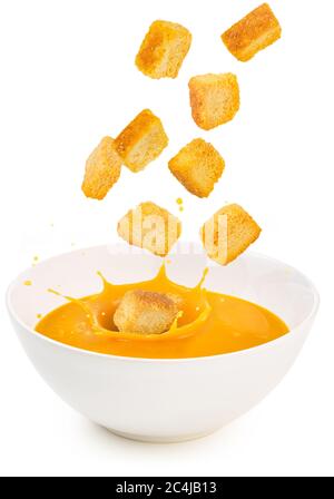 crostini che cadono in una zuppa arancione isolato su bianco Foto Stock