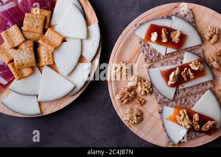 Varietà di piatti di legno con jamon fresco, formaggio e pane arrosto; un formaggio intero e pane tostato con formaggio, noci e gelatina di mele cotogne. Foto Stock