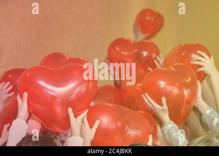 Palline rosse sotto forma di cuori nelle mani dei bambini, foto tonica. Foto Stock