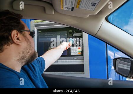 Toronto, Ontario, Canada - 20 giugno 2020: Uomo caucasico sopportato che prende i soldi di contanti dalla macchina del bancomat all'azionamento attraverso la banca. Conducente che utilizza il servizio bancario Foto Stock