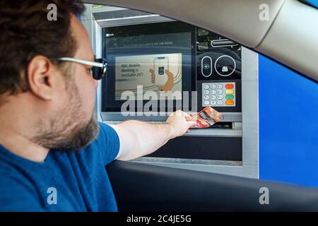 Toronto, Ontario, Canada - 20 giugno 2020: Uomo caucasico sopportato che prende i soldi di contanti dalla macchina del bancomat all'azionamento attraverso la banca. Conducente che utilizza il servizio bancario Foto Stock