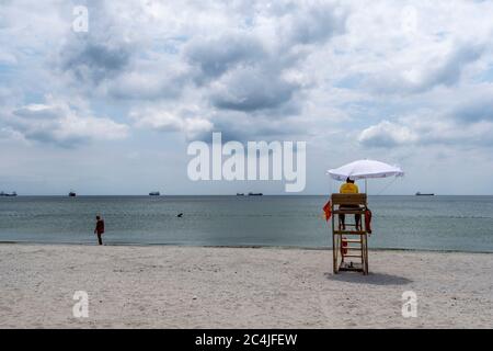 Un bagnino seduto sulla torre di sorveglianza, davanti al mare. Bagnino da spiaggia. Bagnino in spiaggia in servizio. Cielo nuvoloso. Foto Stock