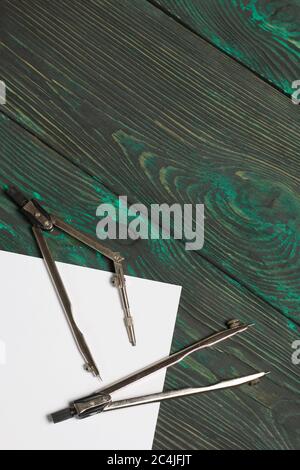 Imposta per il disegno. Due bussole e un foglio di carta bianca. Si trovano su tavole di pino dipinte in nero e verde. Foto Stock