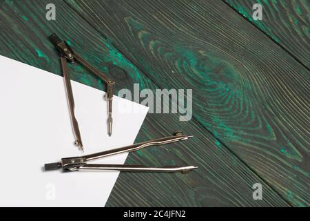 Imposta per il disegno. Due bussole e un foglio di carta bianca. Si trovano su tavole di pino dipinte in nero e verde. Foto Stock