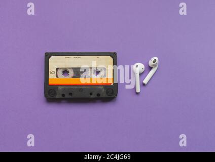 vista dall'alto di una cuffia wireless e di un nastro audio-cassetta sullo sfondo viola. Concetto di evoluzione della musica. Foto Stock