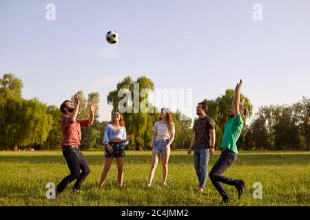 Gruppo di amici che si divertono giocando con una palla su un picnic in erba in un parco estivo. Foto Stock