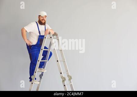 Costruttore divertente uomo worker.deliziato costruttore maschile su scala metallica. Foto Stock