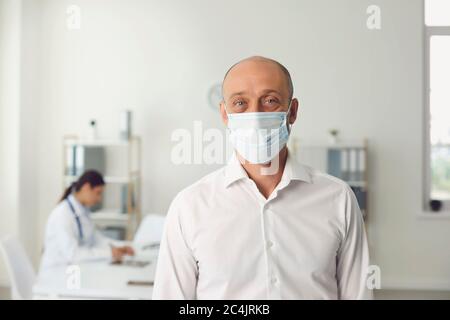Uomo anziano che indossa una maschera protettiva in visita al medico in ospedale, spazio vuoto. Paziente e specialista medico in clinica Foto Stock