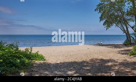 Giovane coppia da sola su una striscia di spiaggia sabbiosa sul lago Ontario, Canada. Splendida vista sull'acqua da un'ampia distesa di spiaggia di sabbia. Spiaggia del tramonto. Foto Stock