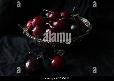 Ciliegie dolci mature fresche su piatto rustico su fondo nero. Foto Stock