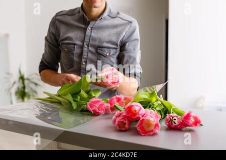 Negozio di consegna fiori. Fiorista che crea ordine, facendo bouquet di primavera. Maschio fare bouquet con tulipani Foto Stock