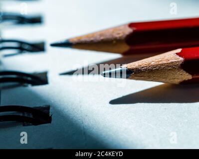 Primo piano di due matite che puntano verso un raccoglitore ad anello parzialmente illuminato dalla luce solare Foto Stock