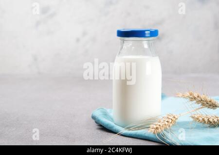 Bottiglia singola di latte in vetro con asciugamano blu e orecchie di grano su un tavolo Foto Stock