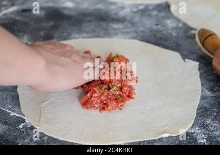 Una donna sta facendo una pizza turca tradizionale (lahmacun). Concetto di cucina casalinga, cottura a casa. Foto Stock