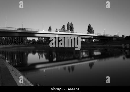 Alla luce del sole che tramonta, il ponte si riflette dall'acqua del fiume (bianco e nero) Foto Stock