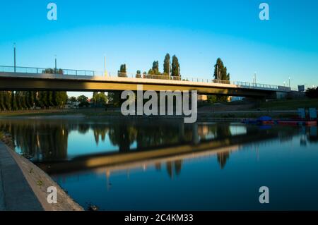 Alla luce del sole che tramonta, il ponte si riflette dall'acqua del fiume Foto Stock