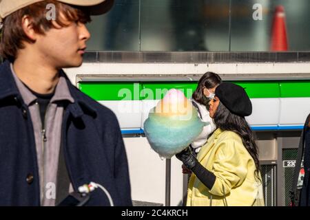 Una giovane donna nera alla moda che mangia un coloratissimo filo di candela ad Harajuku. Tokyo, Giappone. Foto Stock