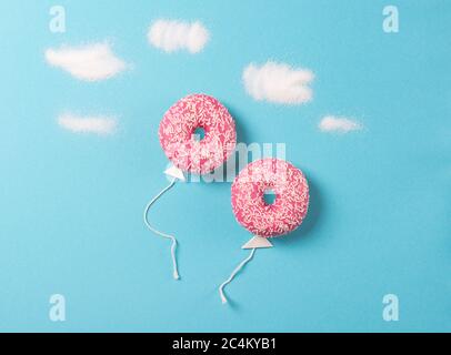 Ciambelle rosa su sfondo blu, minimalismo creativo alimentare, ciambelle a forma di palloncino nel cielo con nuvole di zucchero, vista dall'alto Foto Stock