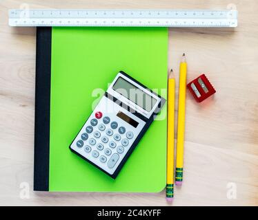 torna a scuola - 2 matite gialle, un affilatore a matita rossa, un notebook verde, una calcolatrice e un righello a tre lati su una scrivania in legno con spazio per la copia Foto Stock