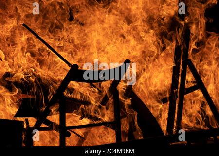 Vista mozzafiato delle fiamme luminose di un fuoco che brucia sedie e oggetti in legno in un edificio Foto Stock