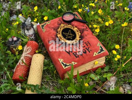 Libro di streghe rosse con candele sull'erba in giardino. Sfondo esoterico, gotico e occulto con oggetti magici, mistico e fiaba concetto outdo Foto Stock