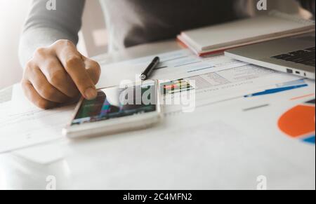 Donna d'affari analizza il grafico di rapporto di affari e grafico finanziario usando lo smartphone e il laptop del calcolatore all'ufficio corporativo. Foto Stock