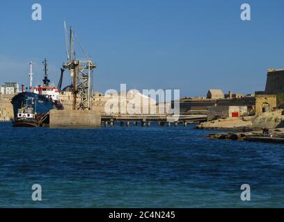 KALKARA, MALTA - 19 aprile 2014: L'industria di impianti di pulizia delle navi cisterna a Rinella Bay, Kalkara, parte di Fort Ricasoli, Malta, in funzione con il mare blu Foto Stock