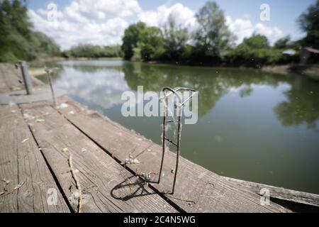 Immagine della profondità di campo (fuoco selettivo) poco profonda con un vecchio supporto metallico inutilizzato per canne da pesca su un molo di legno. Foto Stock