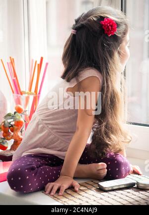 Ragazza riccia dai capelli lunghi seduta sulla soglia della finestra che guarda fuori dalla finestra. Foto Stock