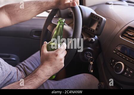 Uomo che guida un'auto mentre tiene una bottiglia di birra. Immersione ubriaca, concetto di guida non sicuro Foto Stock