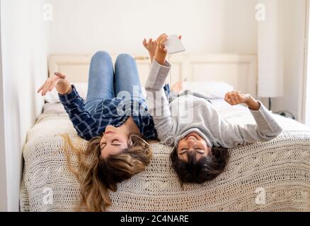 Blocco COVID-19. Ritratto di donne fidate e positive fidanzate ascoltare musica online insieme sul telefono cellulare durante coronavirus sociale dist Foto Stock